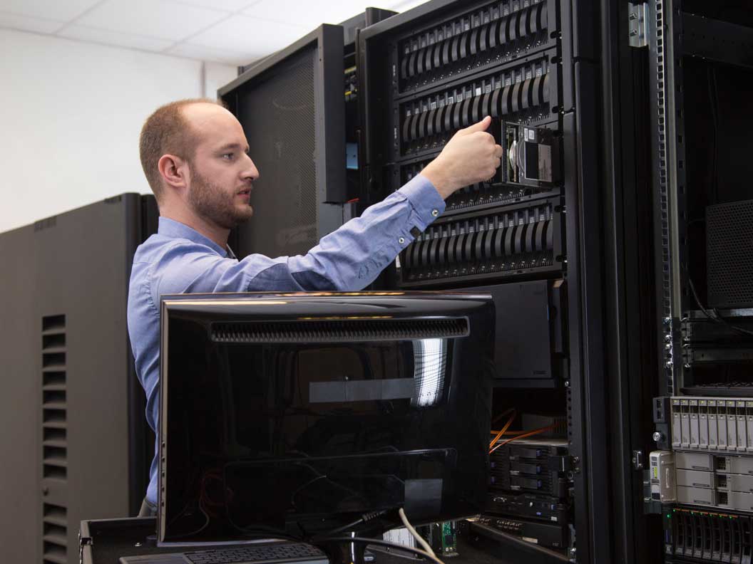 Male computer network support specialist performing maintenance on a large network server. 